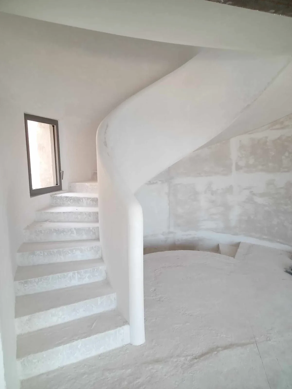 Escalier hélicoïdal maçonné, en cours de finition, éclairé par une fenêtre haute.