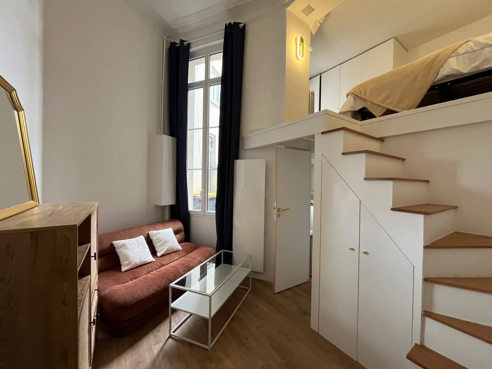 Studio réaménagé : couchage en mezzanine, escalier-rangement et coin salon dessous.