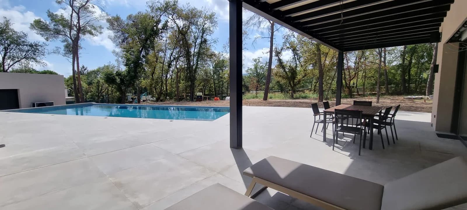 Terrasse et piscine sous une pergola, entourées de pins.
