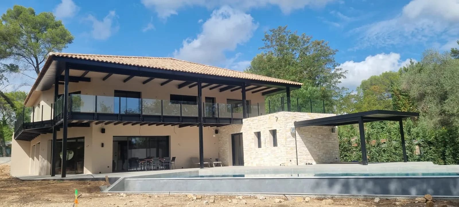 Villa à étage et son bassin, terrasse en pierre claire bordée de pins.